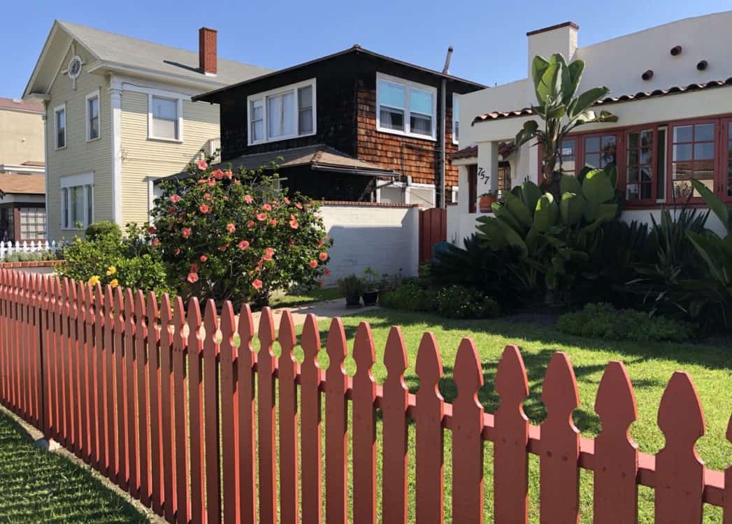 Neighborhood of Coronado - Coronado Island has many beautiful homes. This street is lined with a painted fence. Homes have well manicured landscaping.