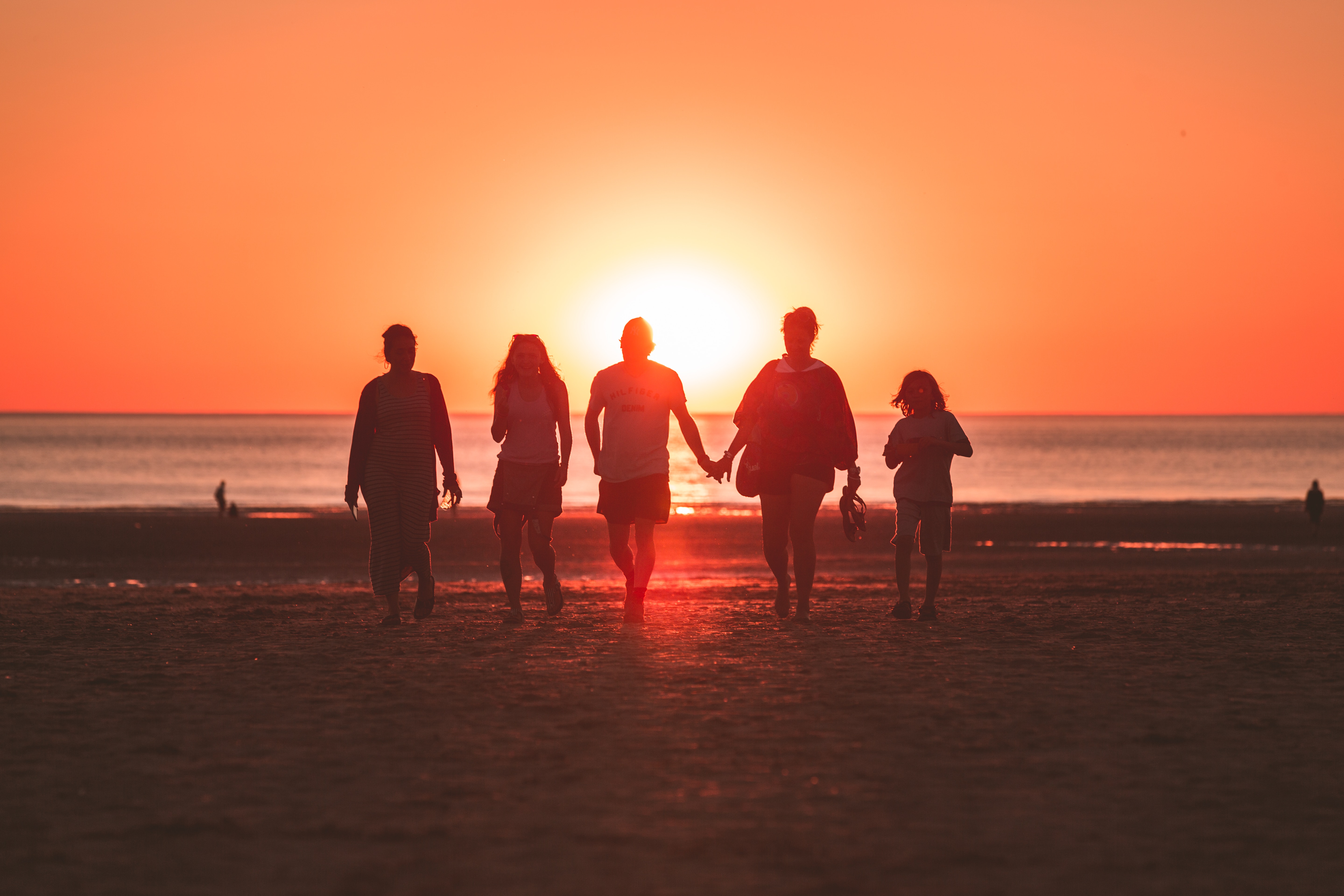 Silhouette photo of five people walking on the beach during sunset.