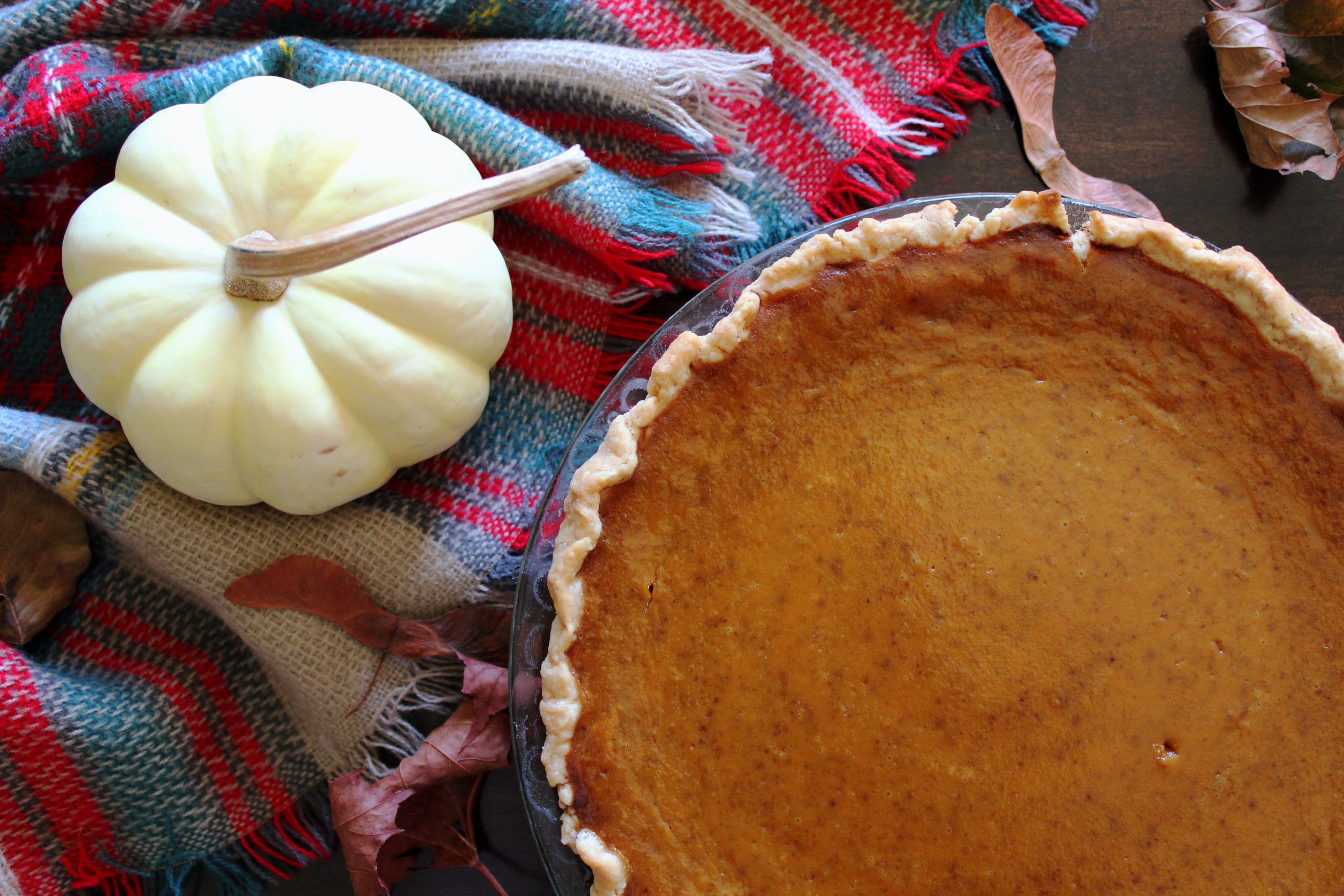 Close Up of a Pumpkin Pie Near a Fake, Cream Gourd, Next to a Tablecloth with Fringe