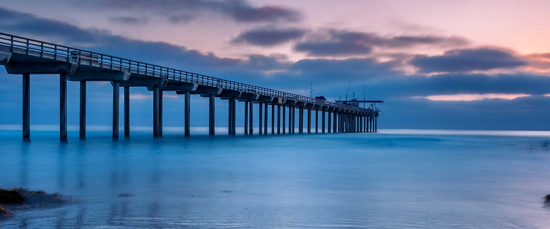 Beautiful scene of a pier in San Diego with a sunset sky and blue ocean waters.