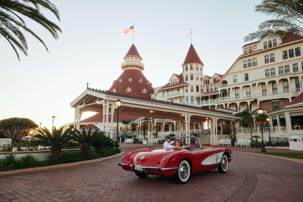 Couple Arriving at Hotel del Coronado in a red and white convertible car driving up the long driveway to the hotel lobby 