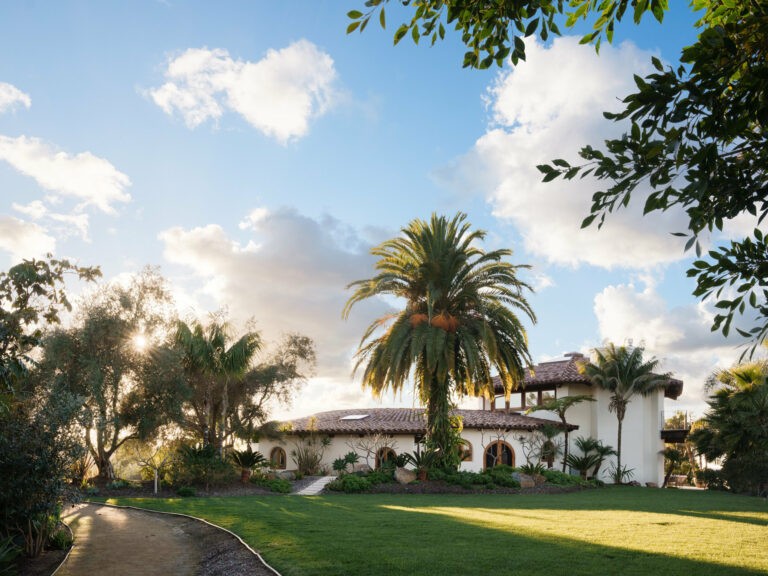 Luxurious Coronado home with sunny driveway and lush lawn, showcasing Spanish revival architecture and distinctive clay tile roof.